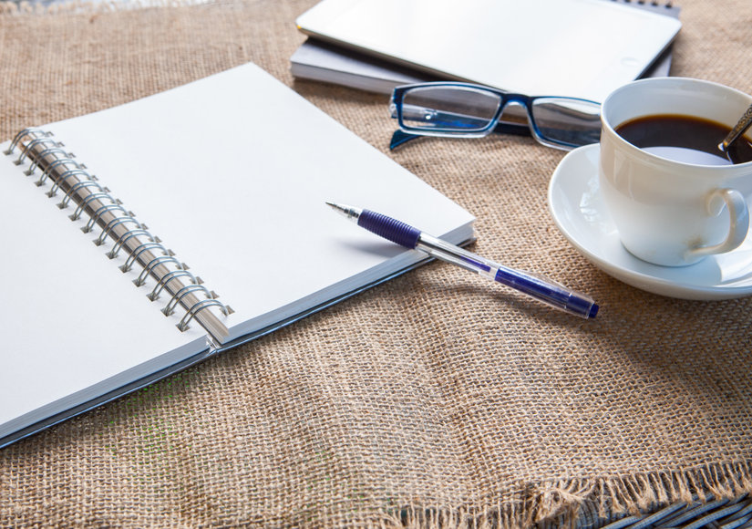 Kaffee, leeres Papier und Stift auf einem Tisch