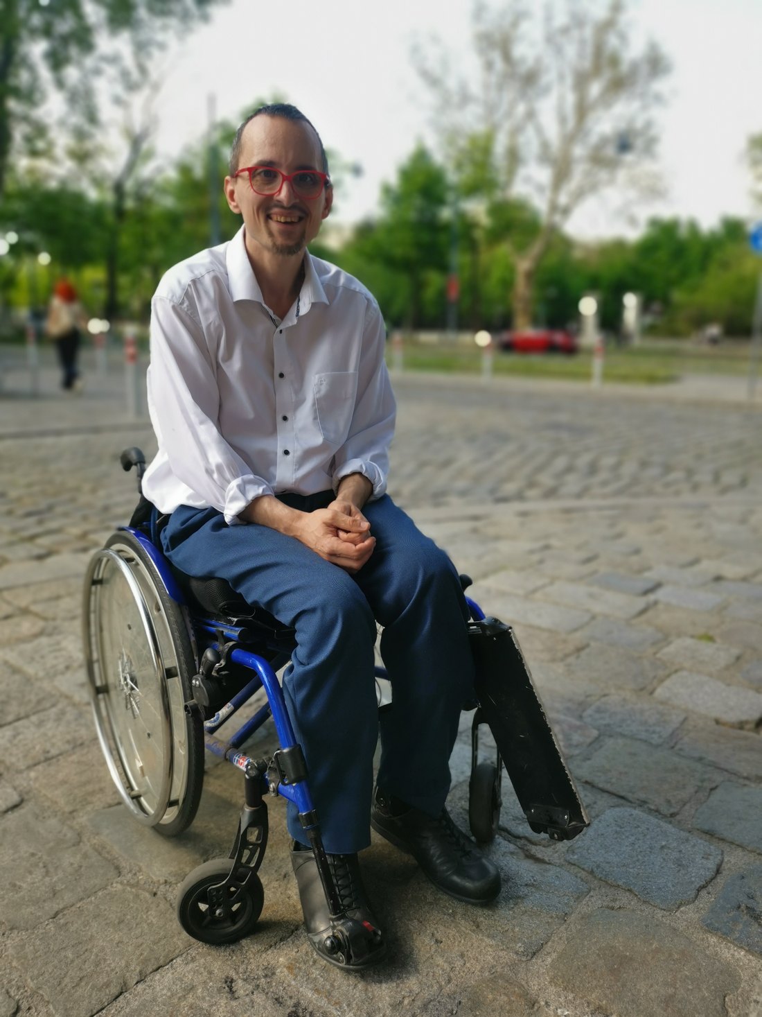 Erwin Strobl sitzt in seinem Rollstuhl auf einer Straße und lächelt
